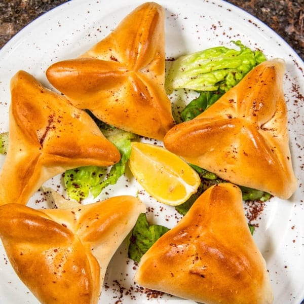 Five golden-brown triangular pastries, likely fatayer, with lettuce and a lemon wedge on a white plate.