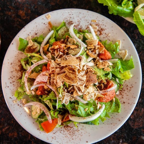 A vibrant Mezza Mediterranean Grille Fattoush salad with lettuce, tomatoes, cucumbers, onions, and pita chips.